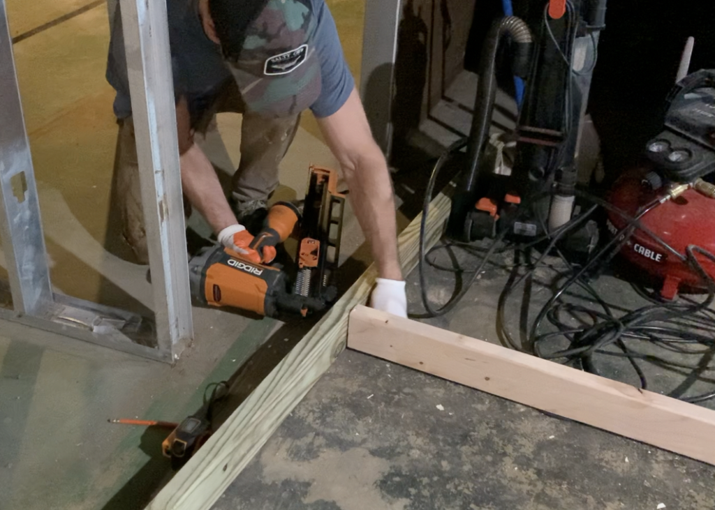 Fasten the basement wall studs to the top and bottom plate with a nail gun